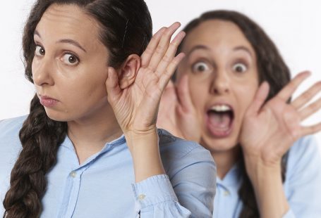 Una ragazza con la mano all'orecchio intenta ad ascoltare mentre dietro un'altra donna si porta le mani alla bocca urlando