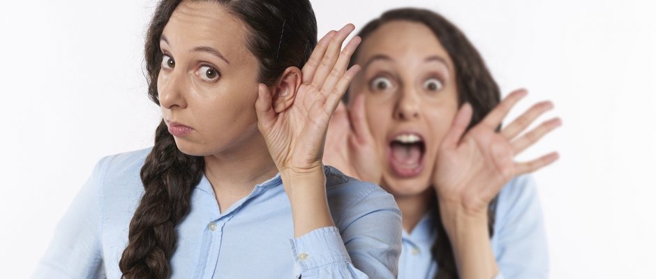 Una ragazza con la mano all'orecchio intenta ad ascoltare mentre dietro un'altra donna si porta le mani alla bocca urlando