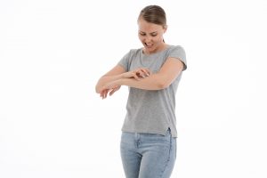 Una giovane donna grattandosi il braccio sinistro con aria infastidita