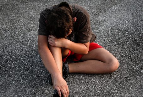 un bambino accovacciato sull'asfalto che si tiene il ginocchio con aria sofferente