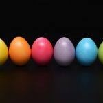 Sei uova di colori diversi messe in fila su sfondo nero