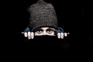 Su sfondo nero, una persona di cui si vedono solo gli occhi, con un cappello di lana infilato in testa che fa capolino 