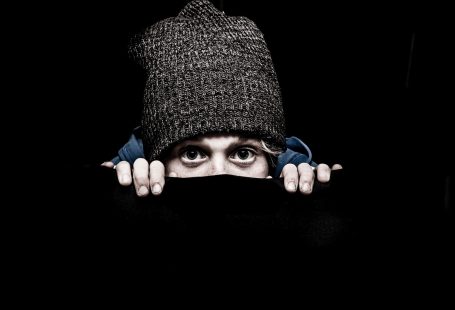 Su sfondo nero, una persona di cui si vedono solo gli occhi, con un cappello di lana infilato in testa che fa capolino
