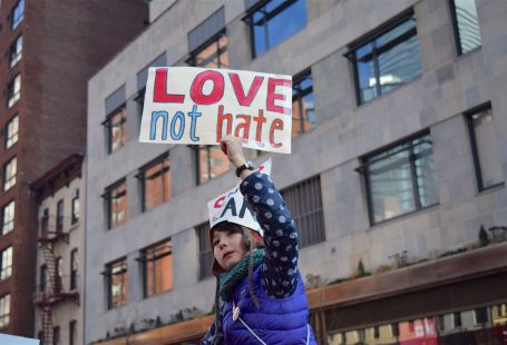 Una bambina con un piumino blu tiene in alto un cartello con su scritto: love not hate
